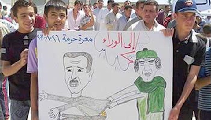 تظاهرکنندگان در سوریه یک کاریکاتور قذافی و بشار اسد را حمل میکنند